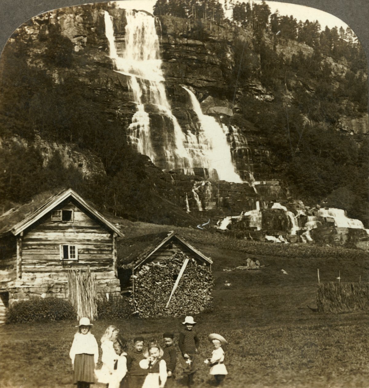 Barn som leker på en bondeåker med terrassert Tvinde-foss, Vossevangen, Norge, c1905. av Unbekannt