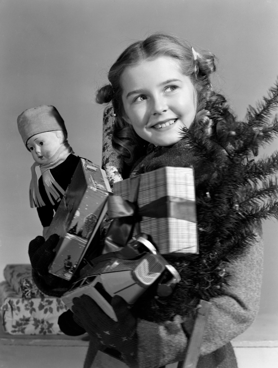 Ung jente bærer en armfull julegaver, ca 1950 av Unbekannt