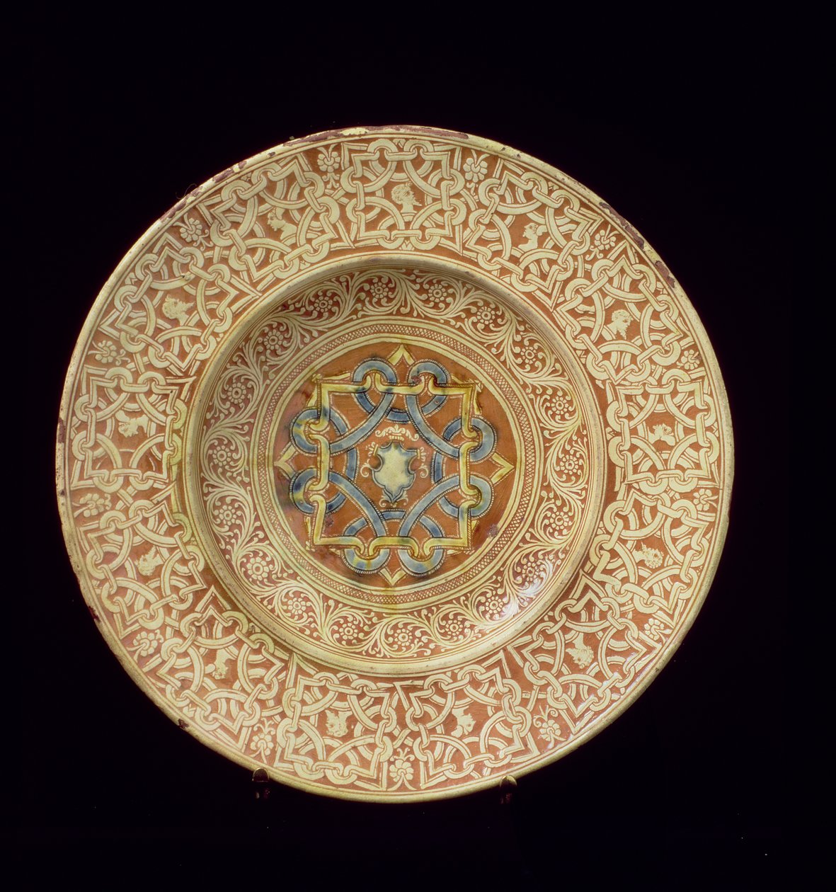 Maiolica-plate dekorert med et forseggjort repeterende knutedesign med innramming av profilhoder på kanten og et skjold i den sentrale plaketten, italiensk, laget i Toscana av Unknown