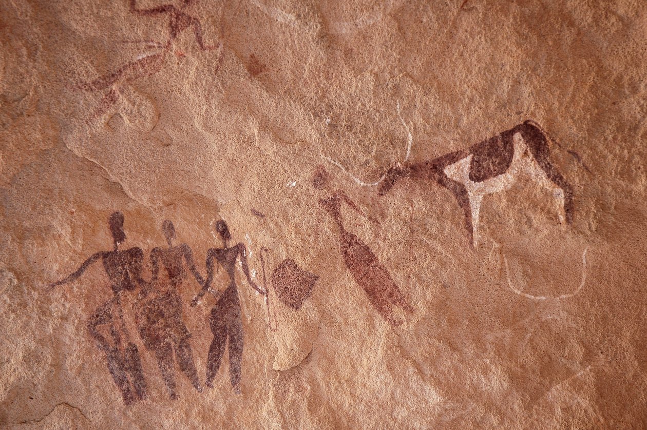 Bergkunst, forhistorie: Bergmaleri av en gruppe karakterer og en tofarget ku med store horn i et utsmykket ly, i Uweinat-massivet, Egypt. (Periode fra 8000 til 3000 år f.Kr.). Fotografering av Unbekannt