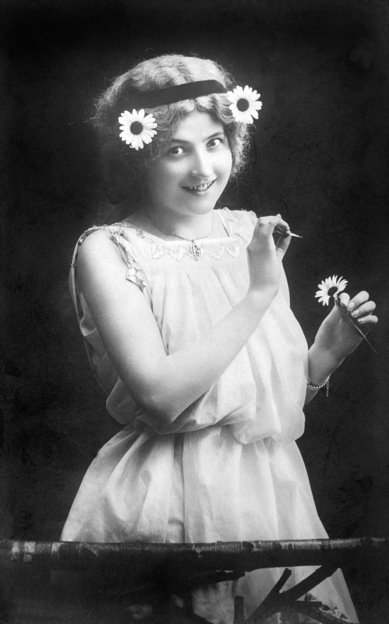 Kvinne som trekker kronbladene fra en blomst: "" Han elsker meg. Han liker meg ikke. Han elsker meg...» Fotografering rundt 1912 av Unbekannt