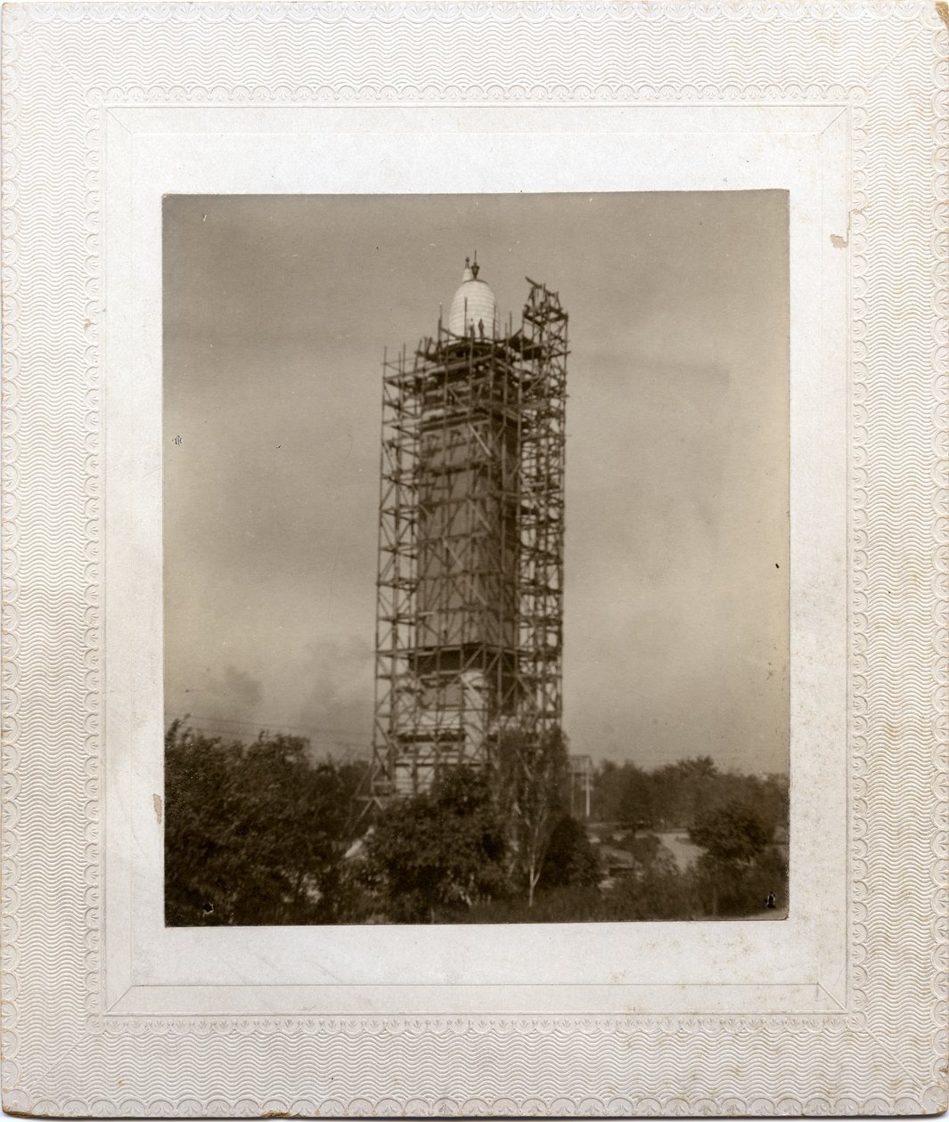 Bygging av Compton Heights Water Tower over eksisterende stårør, med stillaser rundt tårn og arbeider på taknivå. av Unknown