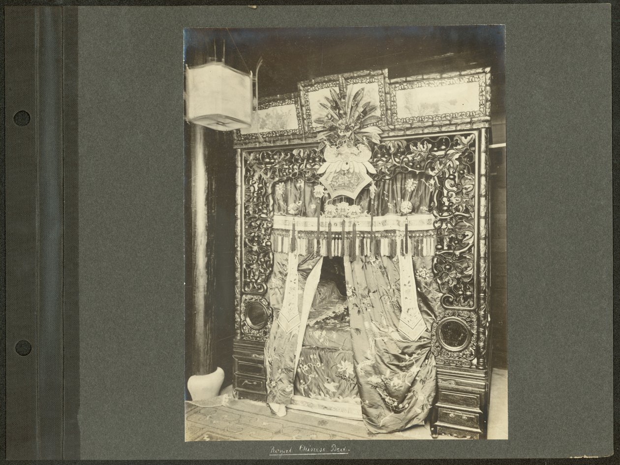 Vertikalt, sepia -fotografi som viser en himmelseng med en forseggjort utskåret sengestolpe i tre og silkeforheng av Unknown