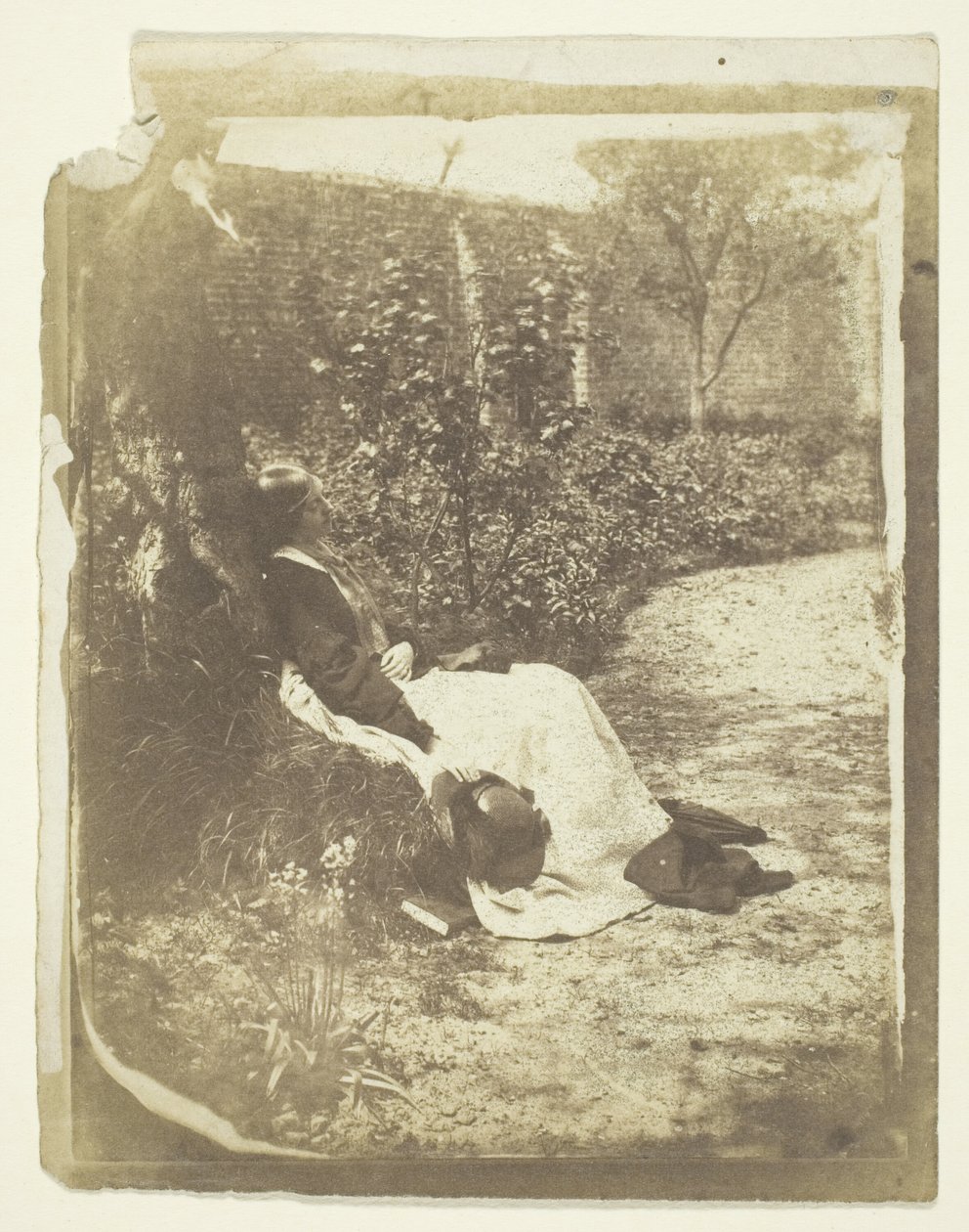 Mrs. Craik liggende i hagen med hatt og bok av Unknown