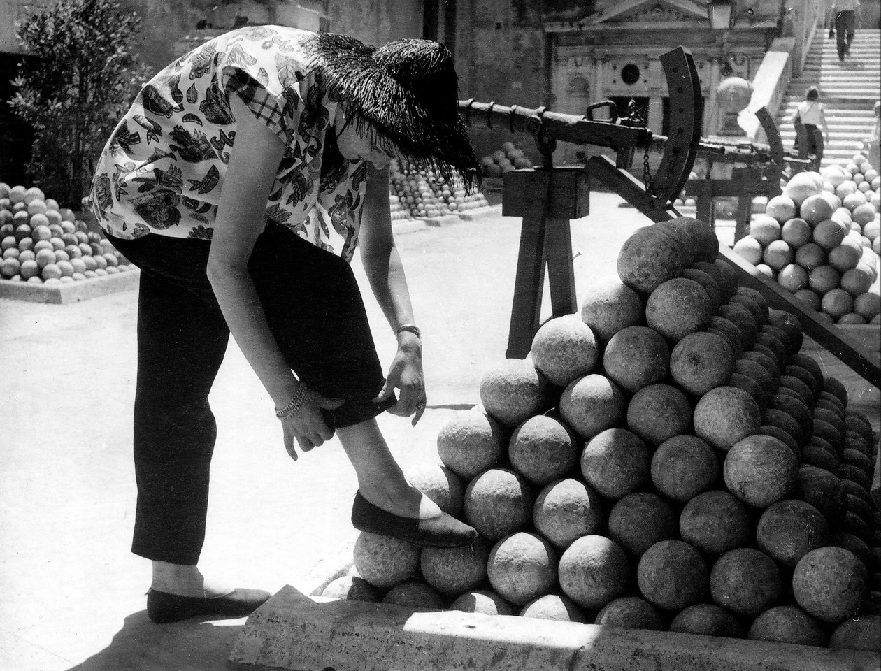 En kvinne justerer mansjetten på buksene mens hun hviler foten på en haug med kanonkuler inne på eiendommen til Castel Sant#39;Angelo i Roma. av Unknown photographer