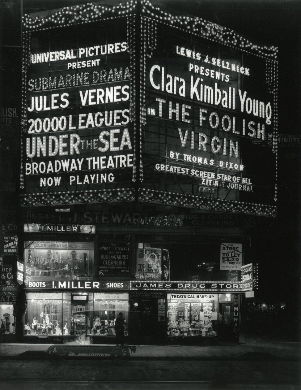 1554 Broadway på 46th Street, I. Miller Shoes; James Drug Store, og store markiser for filmer lyser opp ovenfor. av William Davis Hassler