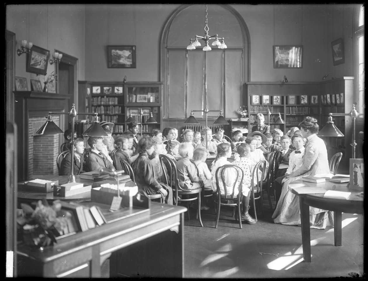 Barn lytter til en kvinne på lesesalen til en uidentifisert filial av Queens Borough Public Library, ca. 1910 av William Davis Hassler