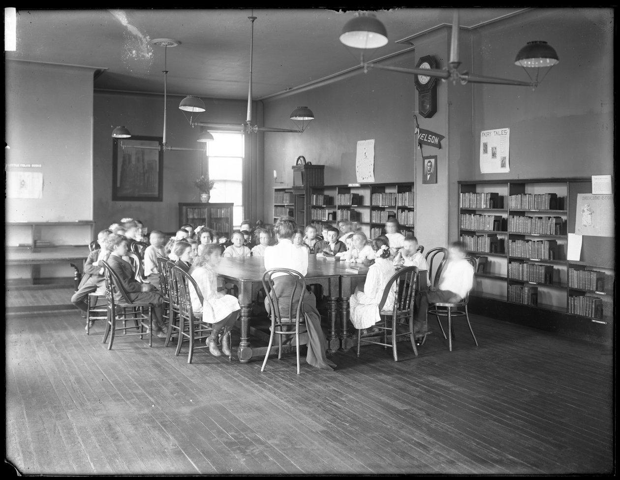 Barn lytter til en kvinne på lesesalen til en uidentifisert filial av Queens Borough Public Library, ca. 1910 (s/hvitt-bilde) av William Davis Hassler
