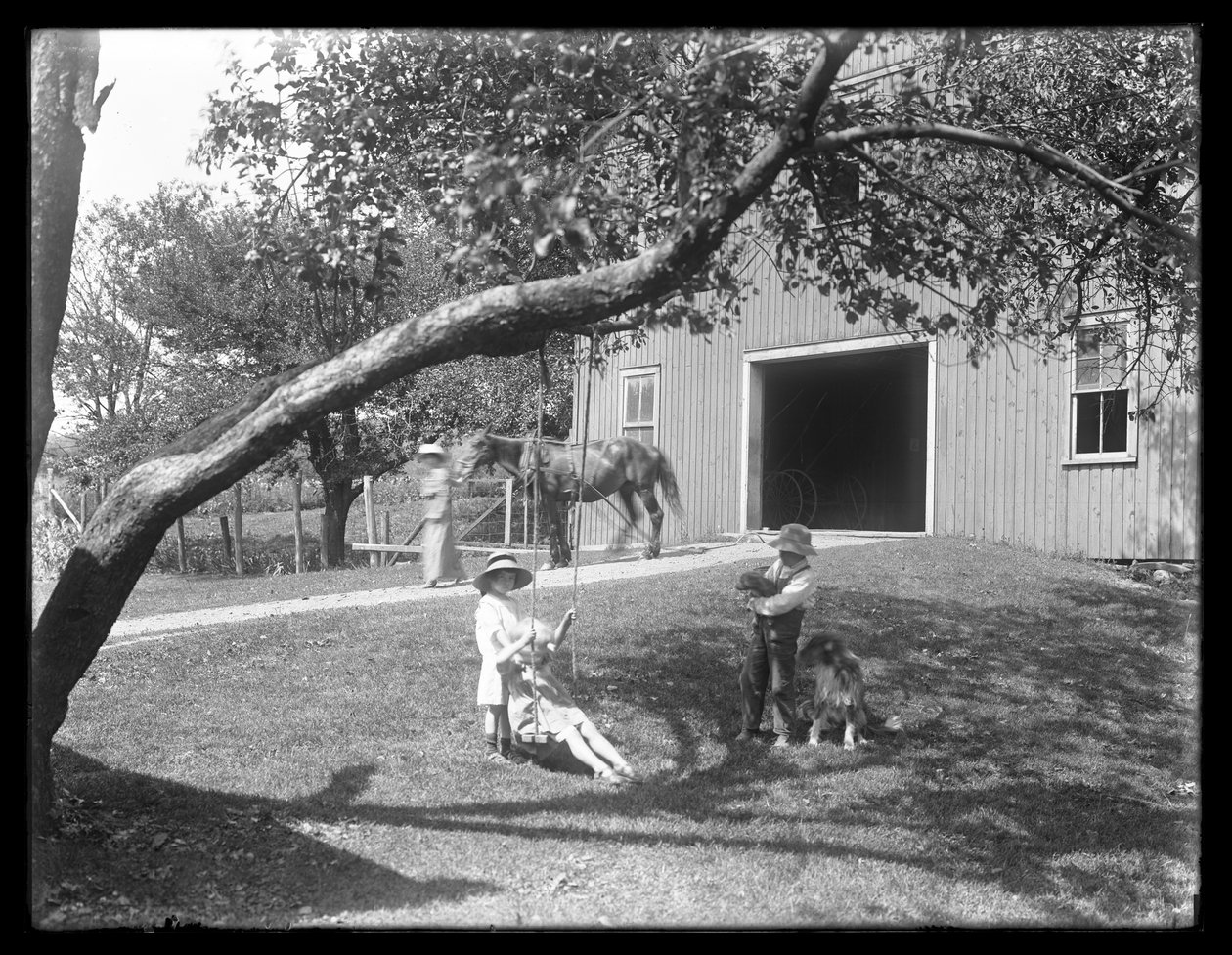 Barn av familien McCready med hund og valp samlet seg rundt en tauhuske utenfor en låve, ca. 1913 av William Davis Hassler