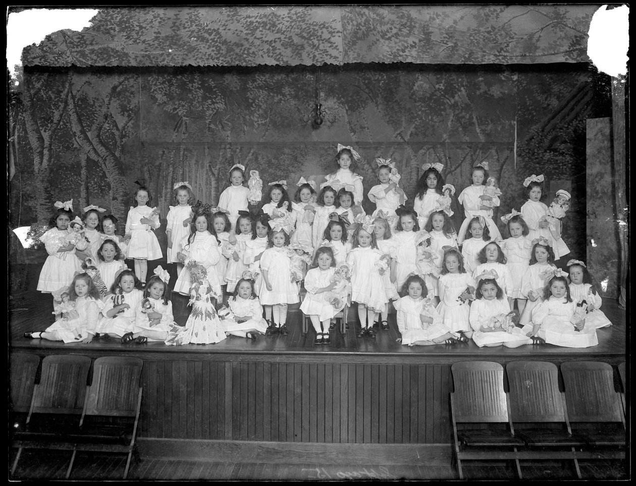 En gruppe små jenter poserte på en liten scene med dukker, sannsynligvis det romersk-katolske orphan asylum, Kingsbridge, Bronx, ca. 1911 av William Davis Hassler