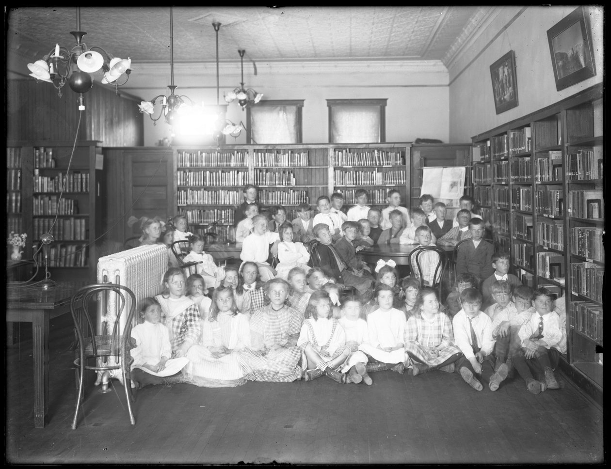 Gruppeportrett av barn på lesesalen til en uidentifisert gren av Queens Borough Public Library, ca. 1910 av William Davis Hassler