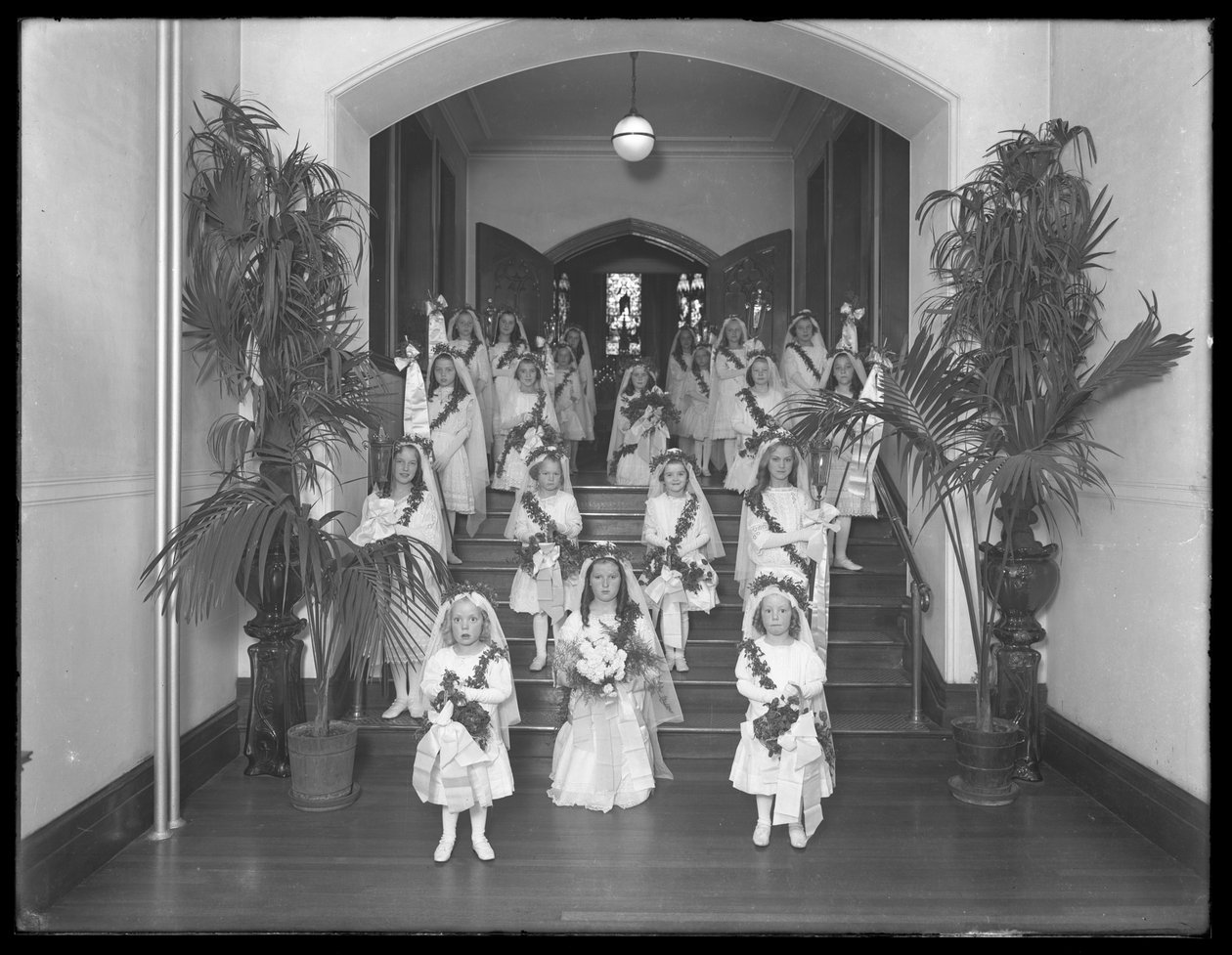 Små jenter på The Roman Catholic Orphan Asylum, Kingsbridge, Bronx, kommer tilbake fra kapellet i hvite kjoler med kranser og kranser, 20. oktober 1914 av William Davis Hassler