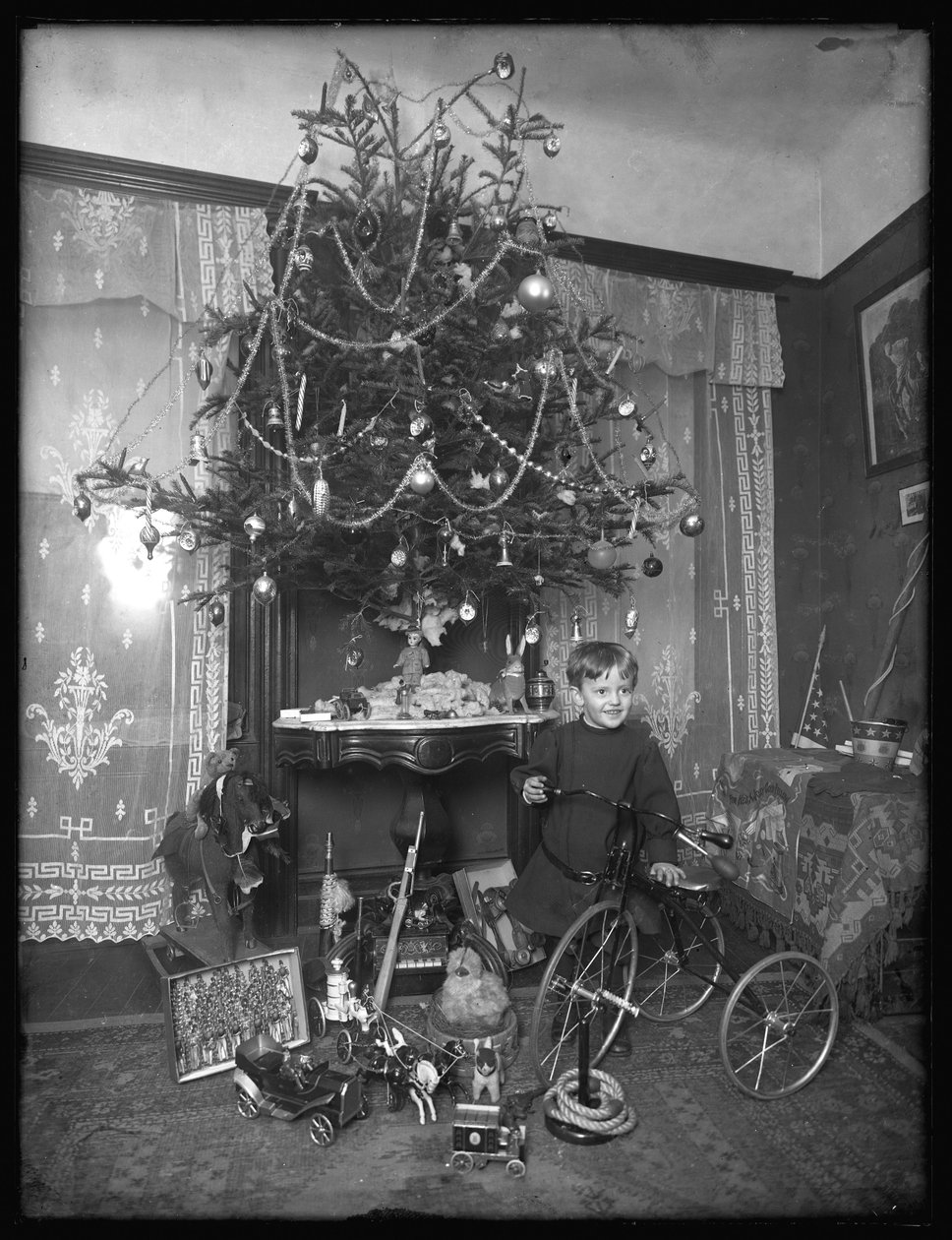 Seymour-gutt poserte med trehjulssykkel ved siden av juletreet i stuen, julen 1912 av William Davis Hassler