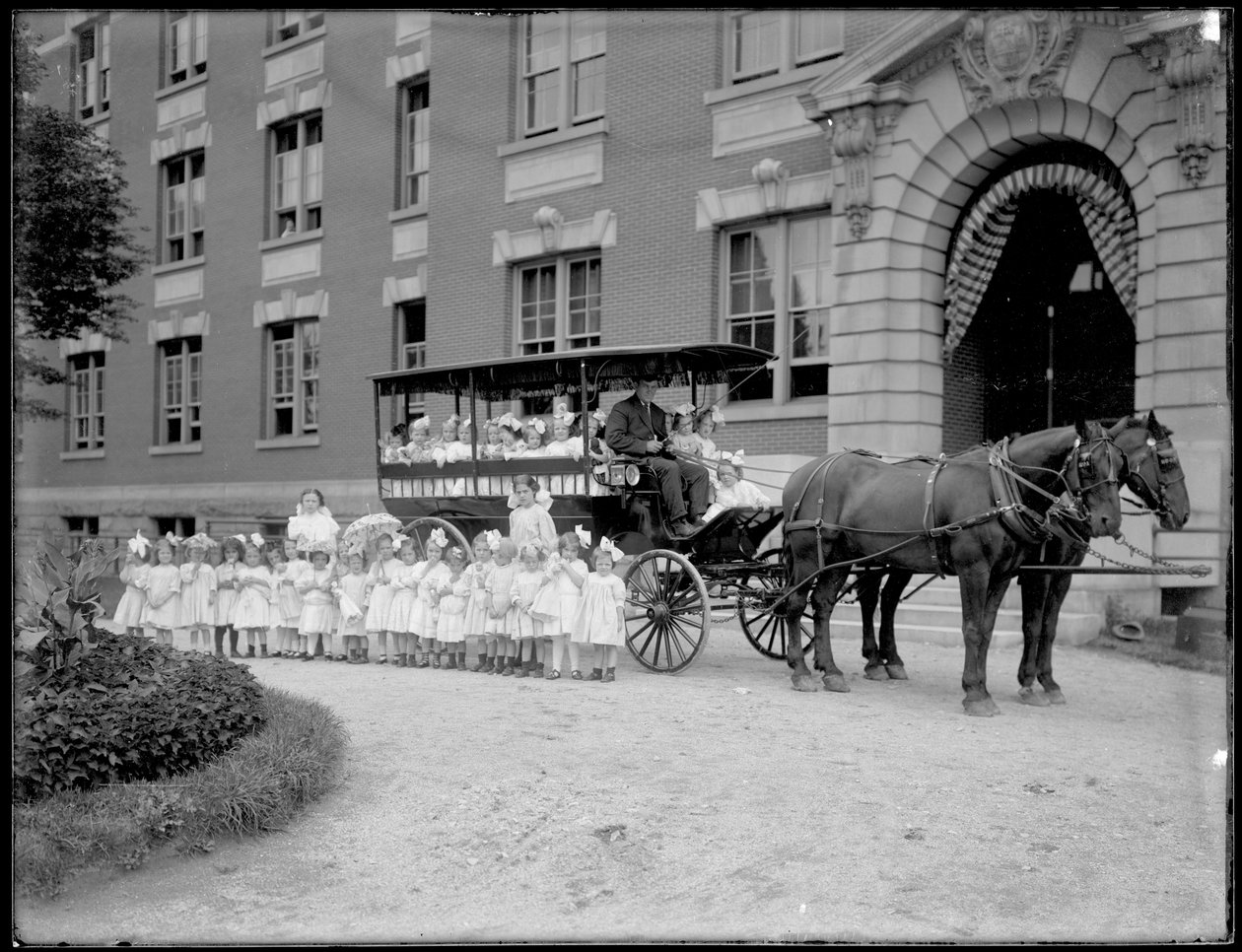 Små jenter poserer i og foran en hestevogn, foran en uidentifisert bygning, sannsynligvis det romersk-katolske orphan asylum, Kingsbridge, Bronx, ca. 1910 av William Davis Hassler