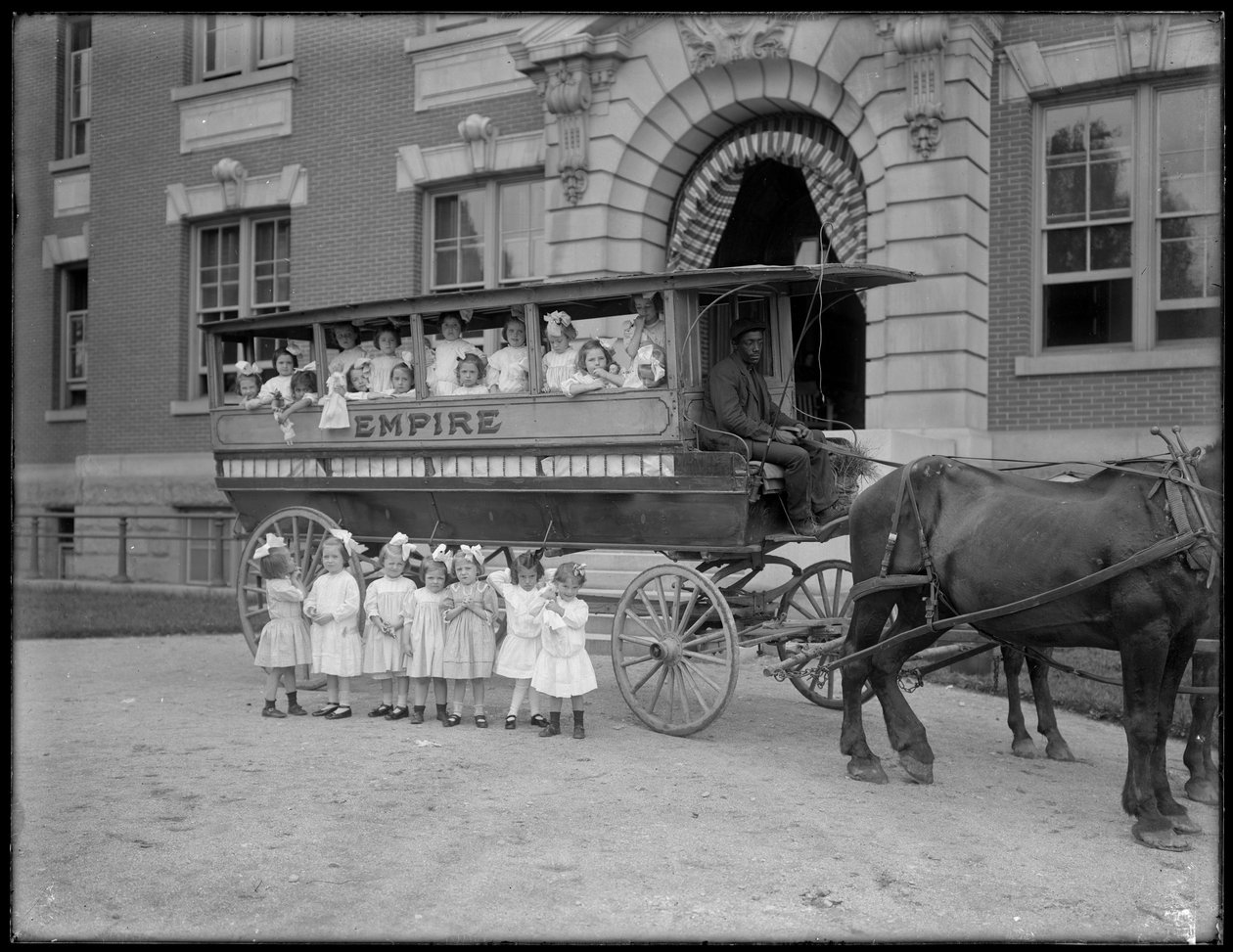 Små jenter poserer i og foran en hestevogn, foran en uidentifisert bygning, sannsynligvis det romersk-katolske orphan asylum, Kingsbridge, Bronx, ca. 1910 av William Davis Hassler