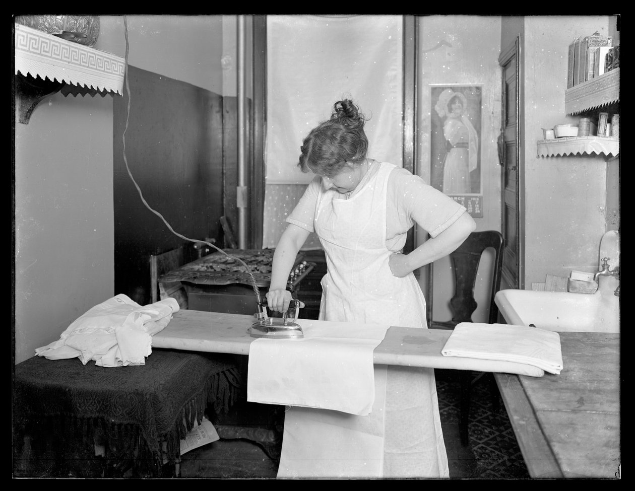 Uidentifisert kvinne demonstrerer bruken av et elektrisk strykejern ca. 1913-14 av William Davis Hassler