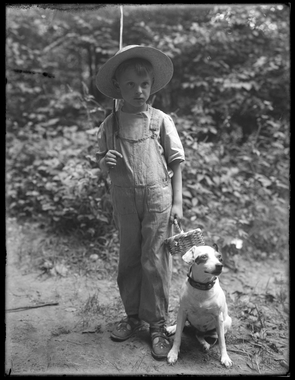 William Gray Hassler i stråhatt og kjeledress, med fiskestang og kurv, poserte i skogen med en liten hund (Bessie), 20. august 1911 av William Davis Hassler