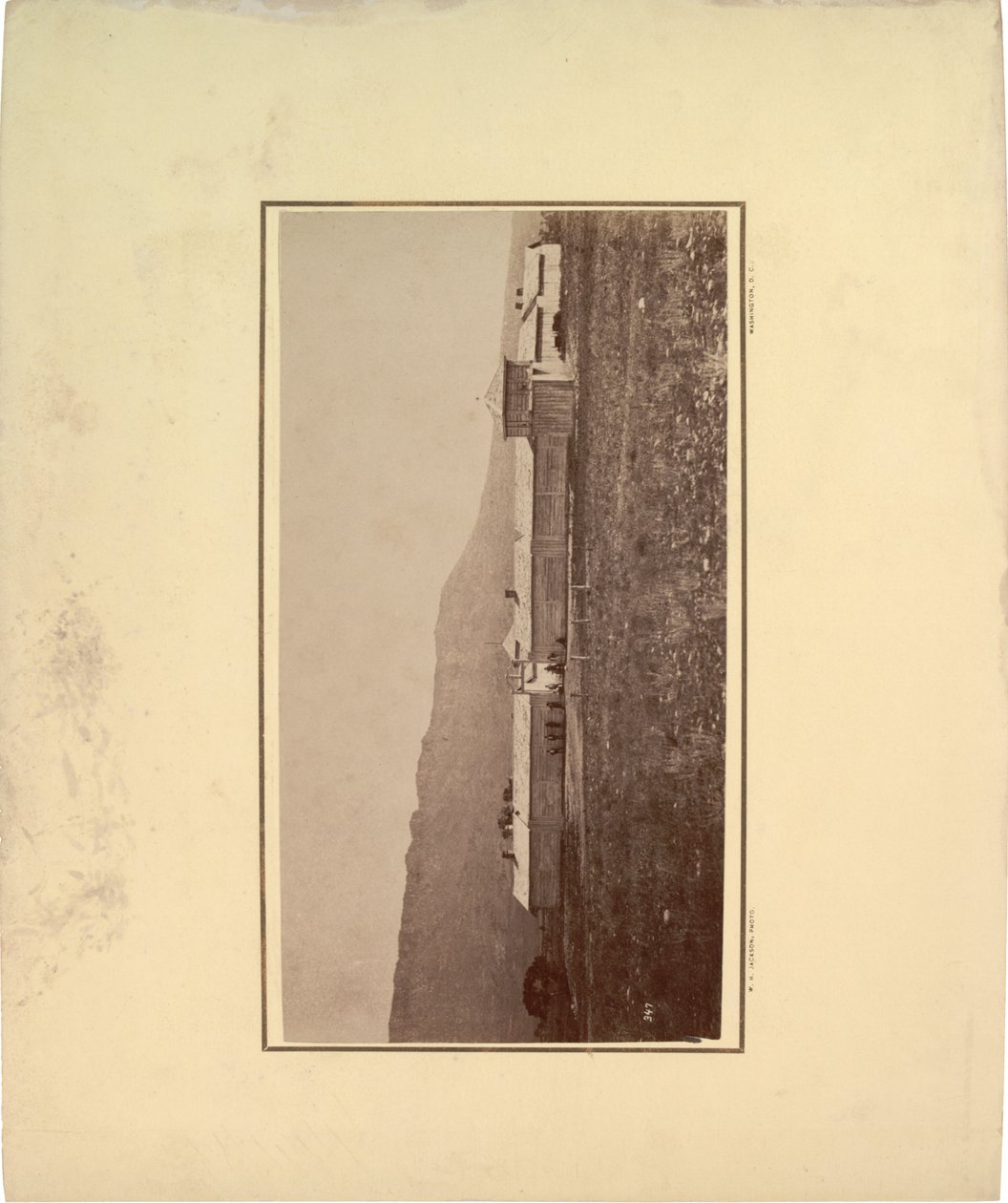 Utsikt over en stockade med flere menn samlet ved inngangsporten, 1871 (sepia-bilde) av William Hicks Jackson