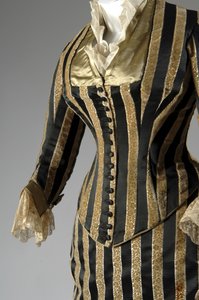 Aftenkjole, ca. 1884 (delvis sideskrå). Silke sateng og kuttet fløyel, blonder, silketråd dusker og frynser. Charles Frederick Worth, Frankrike.