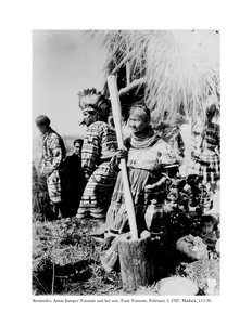 Annie Jumper Tommie bruker en morter og stamper for å lage maismel, og sønnen hennes, Tony Tommie, iført en ørnefjærpanser, 5. februar 1927