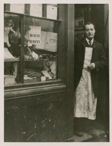 En butikkeier står i døråpningen til butikken hans av English Photographer