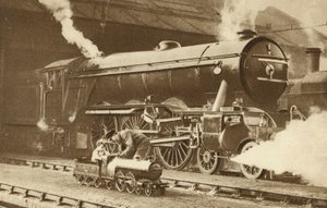 Gutt som kjører et leketøysdamplokomotiv foran det ekte lokomotivet (s/h-bilde) av English Photographer