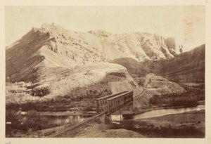 Utsikt over Pacific Railway, av jernbanespor som krysser en elv på en bjelkebro, med fjell utenfor av English Photographer