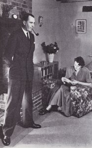 Kona leser, mens mannen varmer ryggen mot bålet, ca.1950 av English Photographer