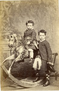 Ung jente på gyngehest med ung gutt i kilt stående, 1860-tallet (albumintrykk)