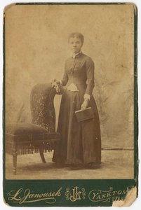 Fotografi av en kvinne som står ved siden av en stol og holder en bok, sent på 1800-tallet. av Louis Janousek