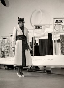Modell i overtrekk laget av couture-huset "Lamma". Artikkelen er samlet i midjen av et bredt sjas, og kompletteres med en myk lue. Bildet er tatt i en hall brukt til utstilling av stoffer. (s/hvitt bilde) av Luis Bogino