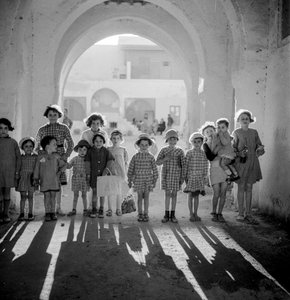 Europeiske barn i skoleuniform under buen med skygger. av Maynard Owen Williams