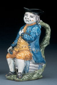 Tobymugge med ansikt og hender i blekt mangan, holdende og tom kulebrunfarget kanne i vasket blå jakke og knebukser, og grønn vest, ca. 1800 av Unbekannt