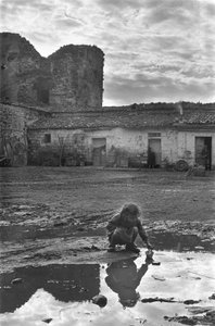 Ung jente leker med en papirbåt i en sølepytt omgitt av gjørme, Venosa, Basilicata, Italia av Unbekannt