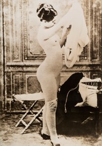 Nakenportrett i helfigur av en ung kvinne som kler seg. av Unknown photographer