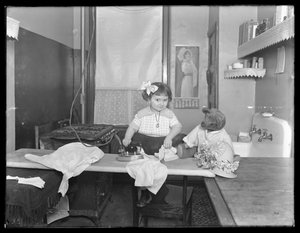 Uidentifisert liten jente som demonstrerer bruken av et elektrisk strykejern, ca. 1913-14 av William Davis Hassler