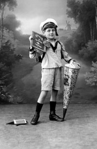 Første skoledag. En ung gutt i uniform poserer med en tavle som viser tillegget 1+1 = 2 og en overraskelsespose. Fotografering rundt 1910. av Ferdinand Georg Waldmuller