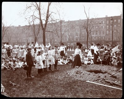 Voksne og barn holder flagg stående rundt et nygravd hull for et treplanting på Arbor Day i Tompkins Square Park, New York, 1904 (sølv gelatintrykk) av Byron Company