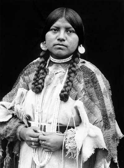 Cayuse kvinne, halvlangt portrett, stående, vendt forover, fletter, skjellskiveøredobber, skallperler og skallperler rundt halsen, perlekledd bukkskinnskjole med perlebelte c. 1910, foto Edward S. Curtis av Edward Sheriff Curtis