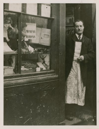 En butikkeier står i døråpningen til butikken hans av English Photographer