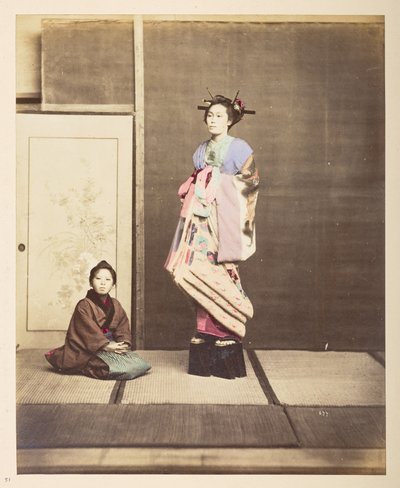 [?Geisha, ] Stående studioportrett i full lengde av en ung kvinne i forhøyede sko, hennes unge ledsager knelende på gulvet ved siden av henne,   Fotograf: Ukjent  Lucas Collection: Fotografisk oversikt over verdensturneen til Charles James og Morton P, Luc av English Photographer