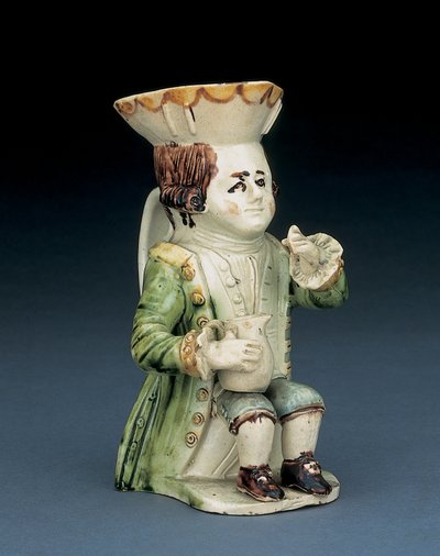 Toper toby kanne, hatten hans med brun og gul kamkant, det innskårne brune håret i kø og med en hvit rosett sittende med en baluster kanne på kneet, ca. 1770 av English School