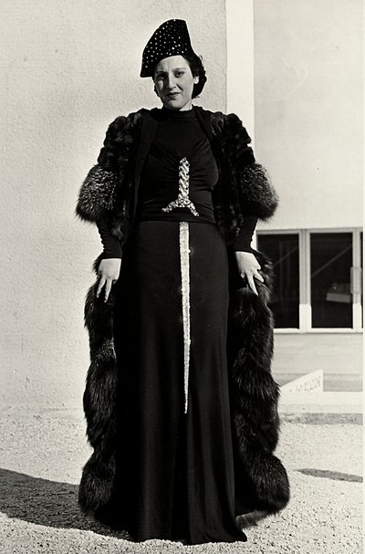 Modell i kveldskjole skapt av det italienske couturehuset "Dragoni". Skriften på artikkelen har en prangende paljettdekor i form av et sverd. En lue og pelsfrakk fullfører ensemblet. (s/hvitt bilde) av Luis Bogino