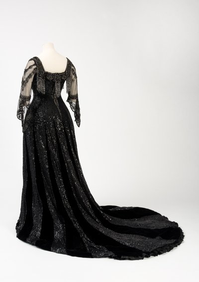 Sort kveldskjole i full lengde båret av dronning Alexandra, med dekorasjon av perler og paljetter og inkorporert dronning Alexandras signaturteip i svart silke og gull, laget av Barolet fra Knightsbridge, London 1908-1910 (silke og fløyel) av Unbekannt