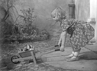 Liten jente leker med en trillebår. Fotografering rundt 1931 av Unbekannt