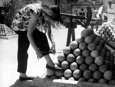 En kvinne justerer mansjetten på buksene mens hun hviler foten på en haug med kanonkuler inne på eiendommen til Castel Sant#39;Angelo i Roma. av Unknown photographer
