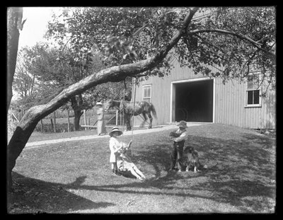 Barn av familien McCready med hund og valp samlet seg rundt en tauhuske utenfor en låve, ca. 1913 av William Davis Hassler