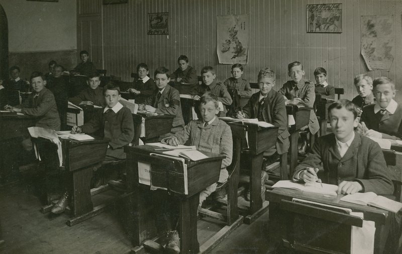 Mannlige elever som sitter bak pultene sine under en leksjon på skolen av English Photographer