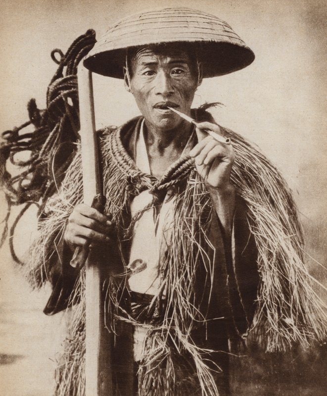 Japansk kulie (gårdsarbeider) med hatt for å beskytte ham mot kraftig regn i rismarkene (s/hv-bilde) av Photographer Japanese