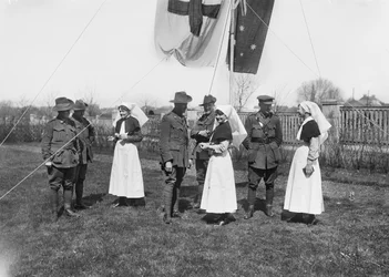 En gruppe uidentifiserte offiserer, sykepleiere og menn fra 3rd Australian Casualty Clearing Station samlet seg under en flaggstang med det australske flagget (Australian Blue Ensign) og Røde Kors-flagget